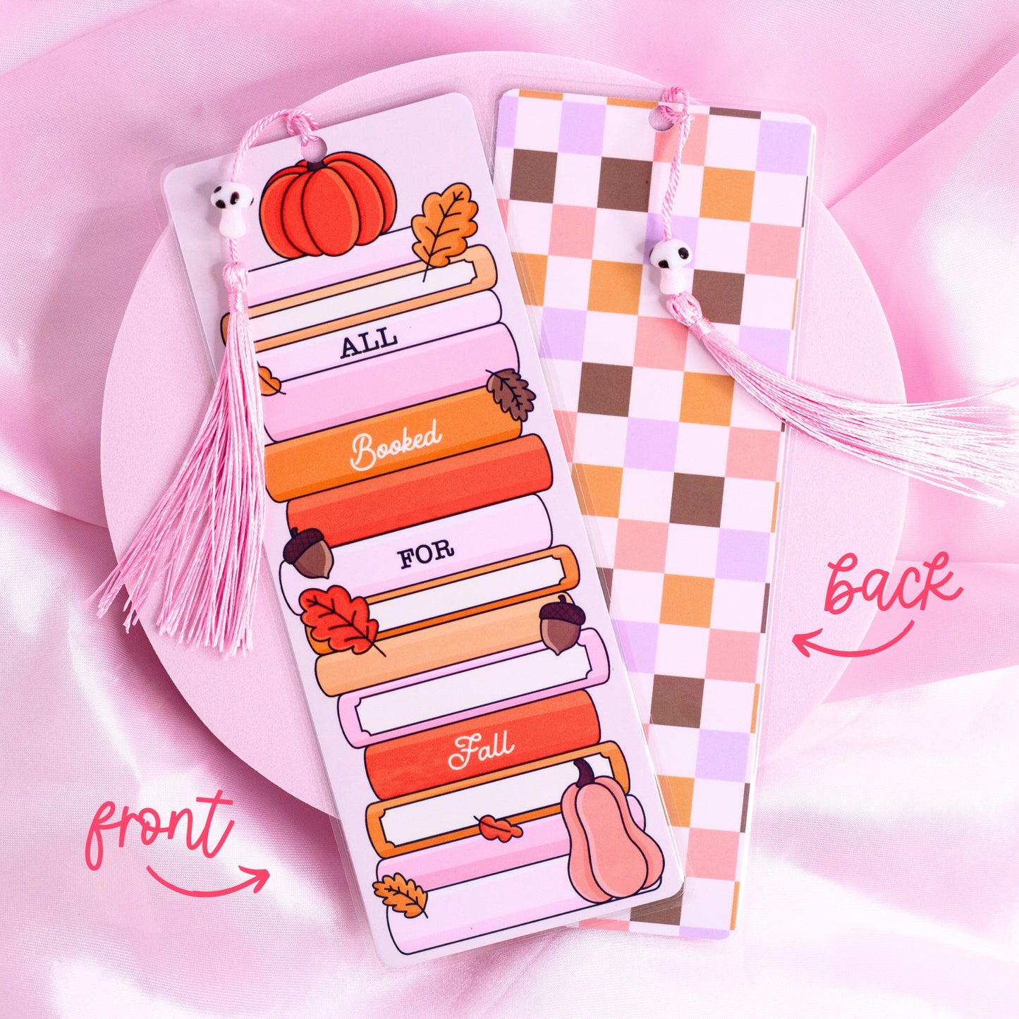 Fall-themed bookmark with stacked pastel books, pumpkin, leaves, and “All Booked for Fall” text, with checkered back design and pink tassel.