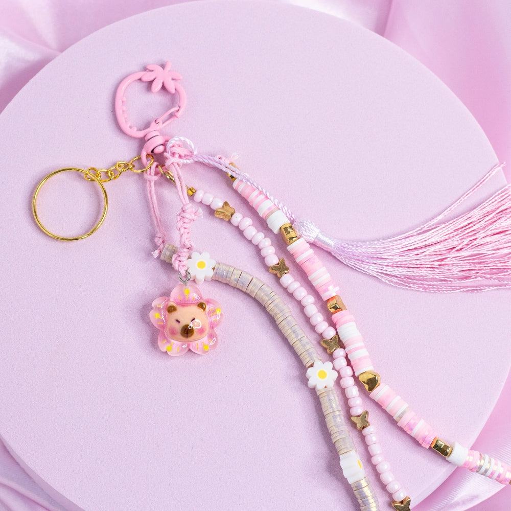 Pink capybara charm keychain with pastel flower beads, gold butterflies, and a pink tassel.