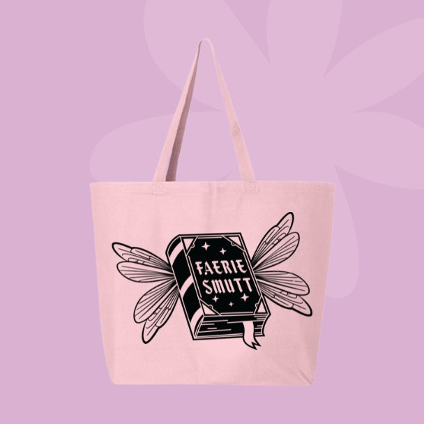 Pink tote bag with a black illustration of a fantasy book with fairy wings, labeled “Faerie Smut.”