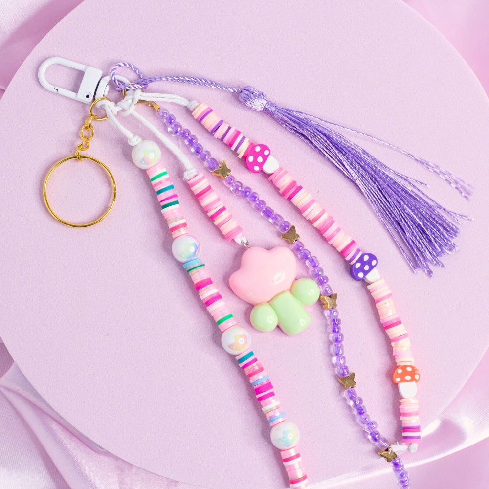 Pink and purple mushroom keychain with floral charm, stripe beads, and lavender tassel.