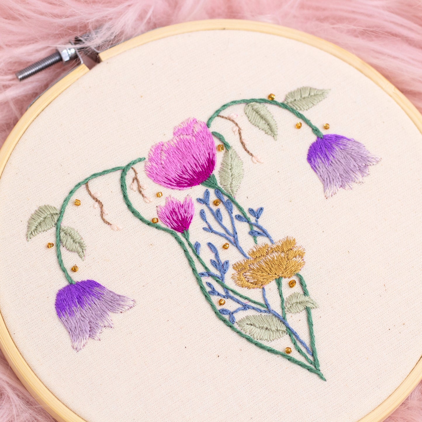 Close-up of floral uterus embroidery hoop art with pink and purple hand embroidered flowers on natural cotton fabric