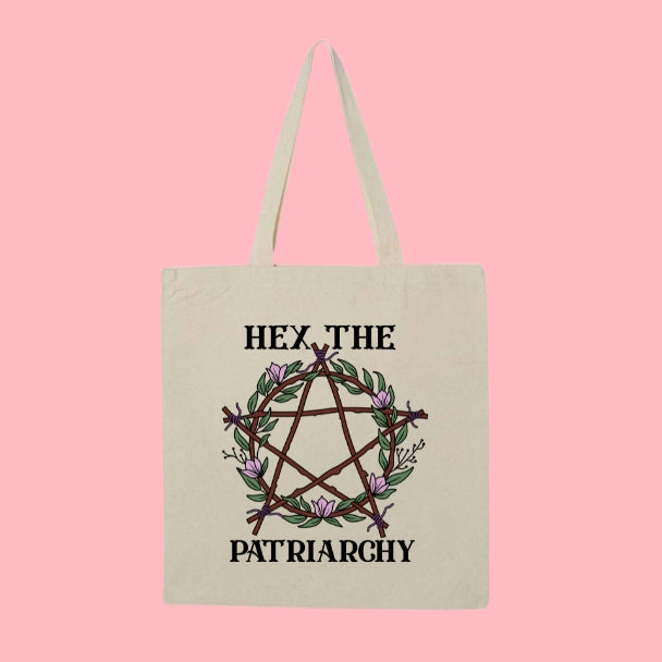 Beige tote bag with a pentagram made of branches and pink flowers, with bold text that says “Hex the Patriarchy.”