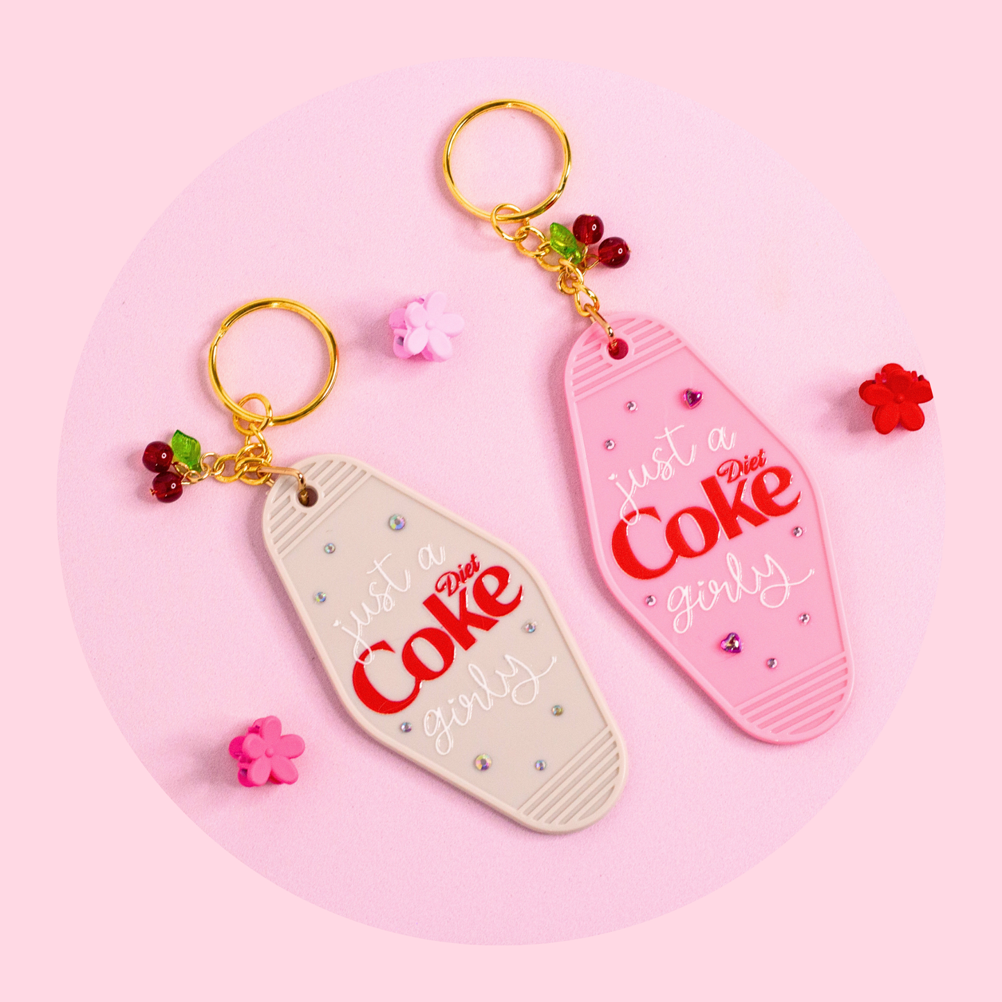 two girly motel style keychains in pink and grey with cherry charms styled on pink surface with small flower clips