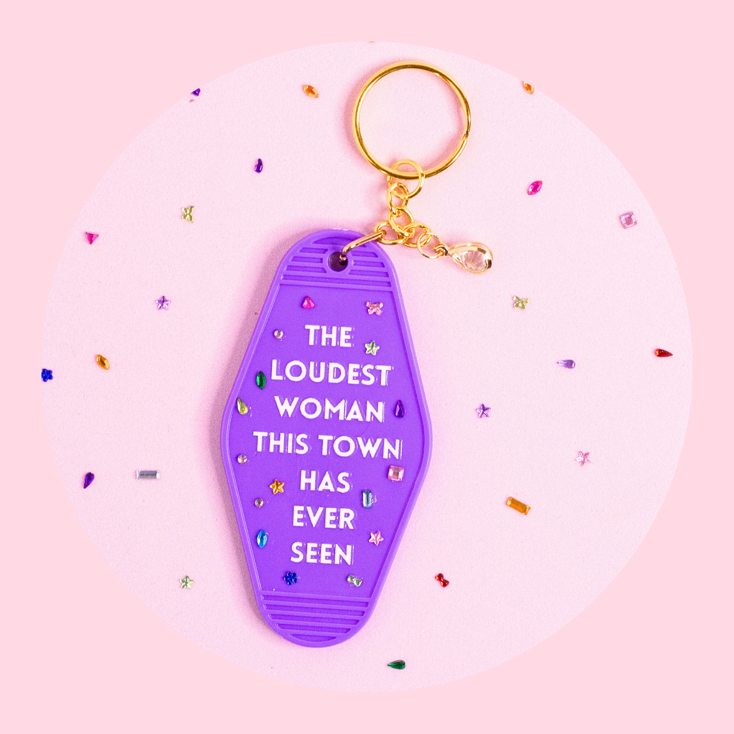 purple motel style keychain with “the loudest woman this town has ever seen” text, rhinestones and gold key ring on pink background