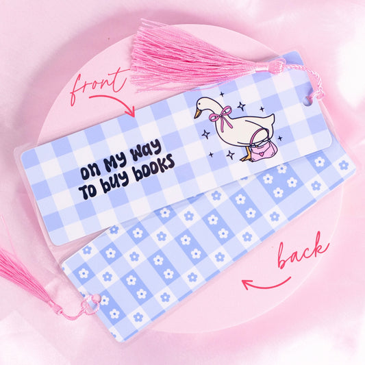 โBlue gingham bookmark featuring a goose carrying a pink purse with the quote โOn my way to buy booksโ โ perfect for bookish adventurers.โ