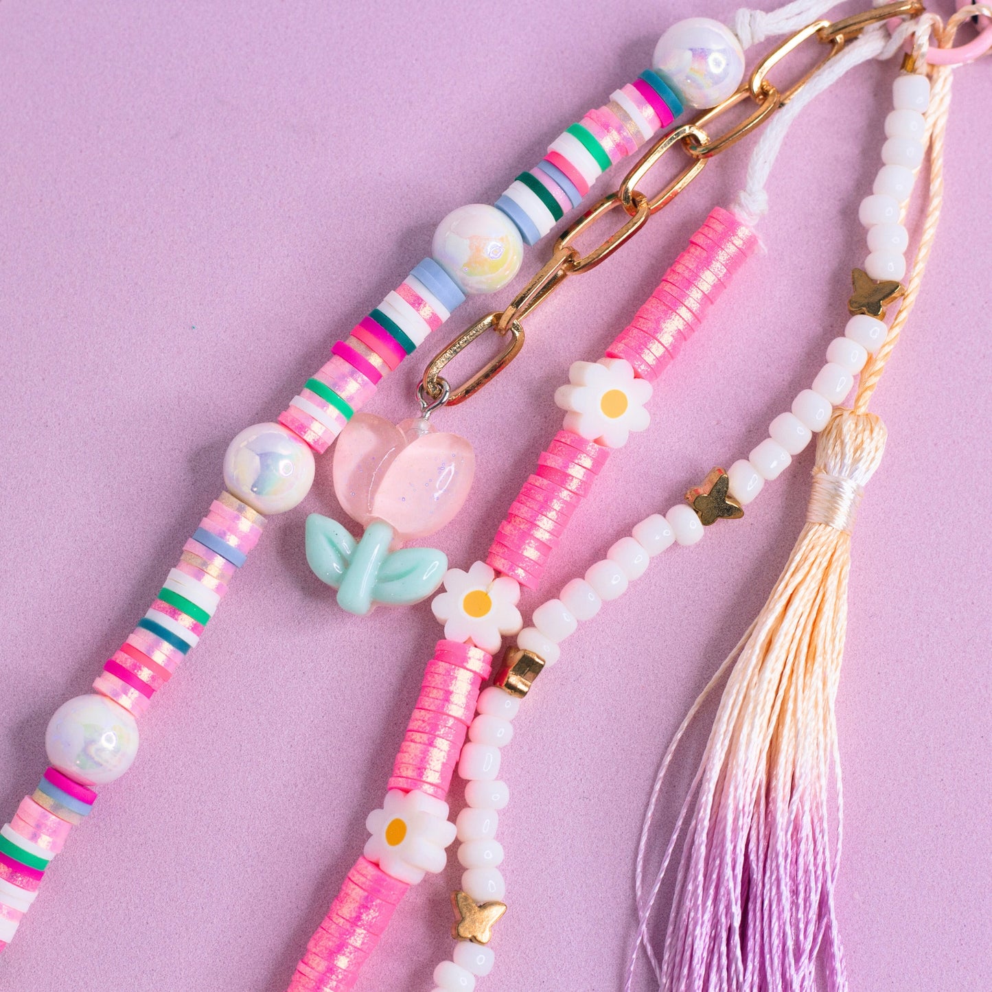 Pink and white purse charm with daisy beads, pastel accents, heart beads, and a purple tassel on a pink clasp close up
