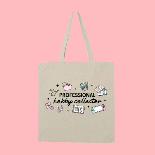 Beige tote bag with doodles of hobbies like painting, knitting, gaming, and reading, with text that says “Professional Hobby Collector.”