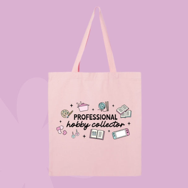 Pink tote bag with doodles of hobbies like painting, knitting, gaming, and reading, with text that says “Professional Hobby Collector.”