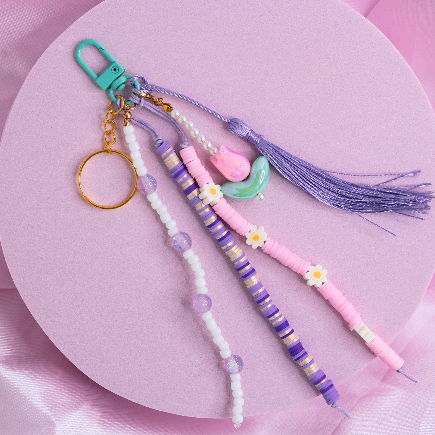 Purple and pink purse charm with striped beads, flower accents, tulip charm, and tassel on a teal clasp.