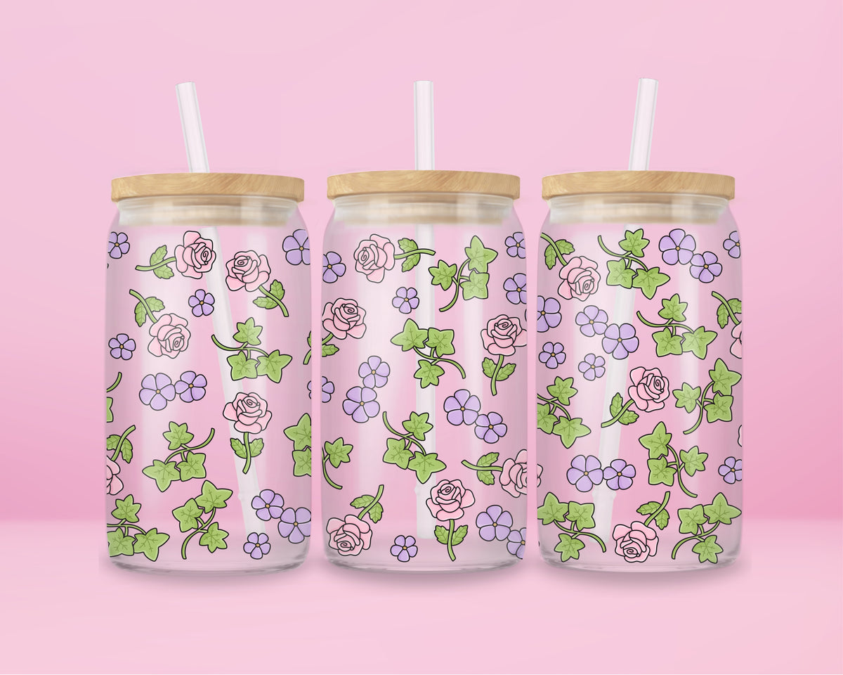 Glass can tumbler with bamboo lid and glass straw featuring pink roses, purple flowers, and green ivy leaves on a pink background.