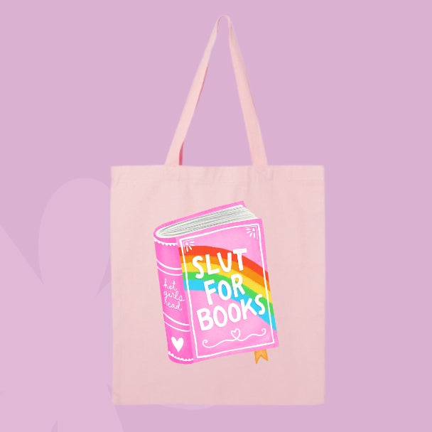 Pink tote bag with a colorful pink and rainbow book illustration that says “Slut for Books.”