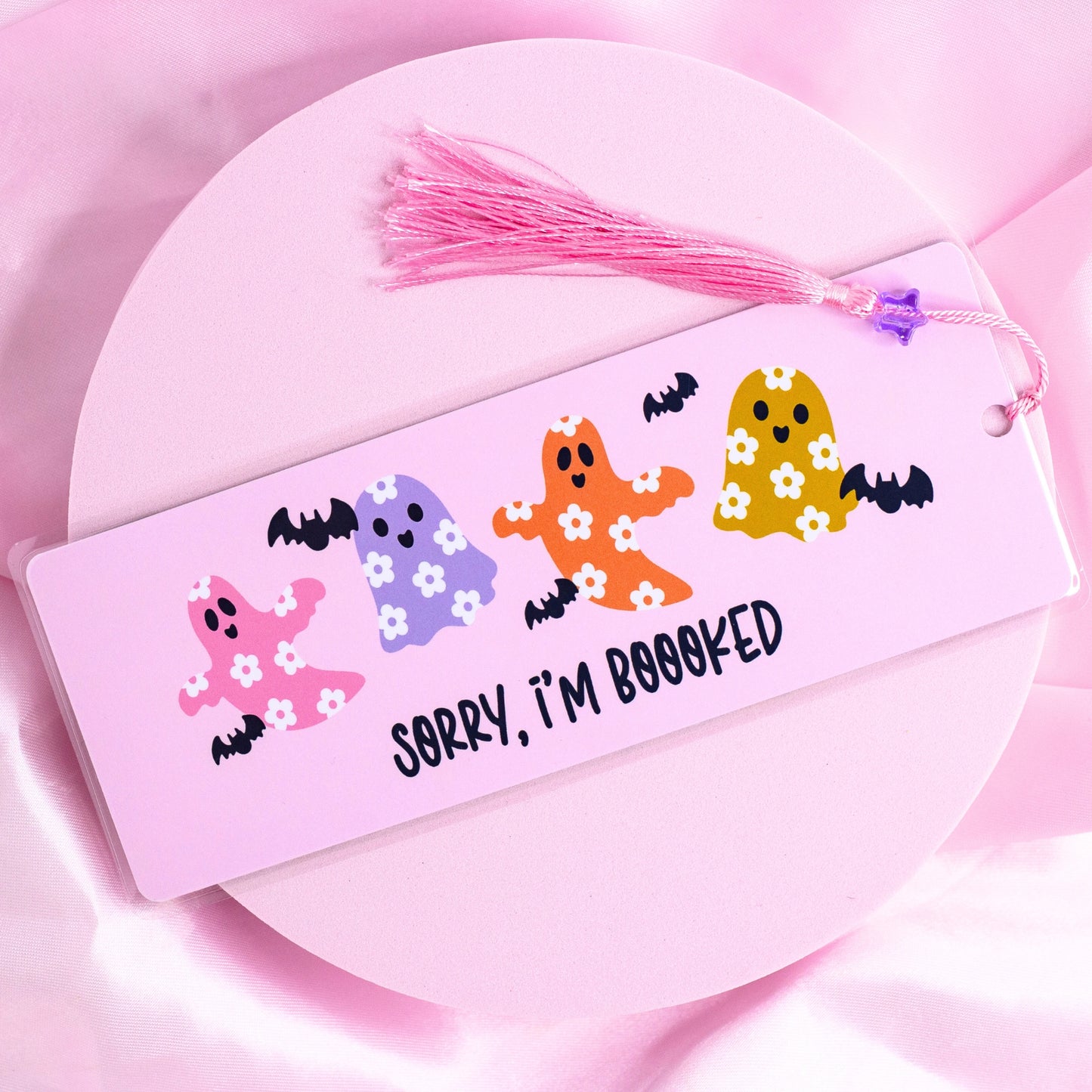 Pink bookmark with colorful flower-print ghosts, bats, and “Sorry I’m Booooked” text, with pink tassel.