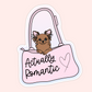 Cute brown dog peeking out of a pink purse with the phrase “Actually Romantic” written on the bag.