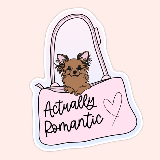 Cute brown dog peeking out of a pink purse with the phrase “Actually Romantic” written on the bag.
