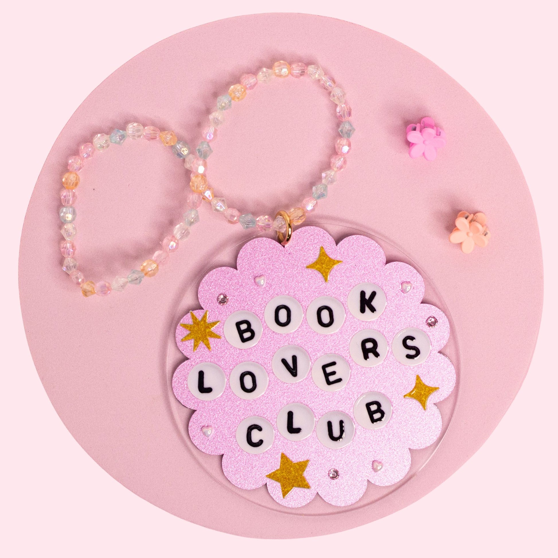 Book Lovers Club car charm featuring a glittery pink acrylic charm with letter beads, gold stars, rhinestones, and a pastel beaded hanger.
