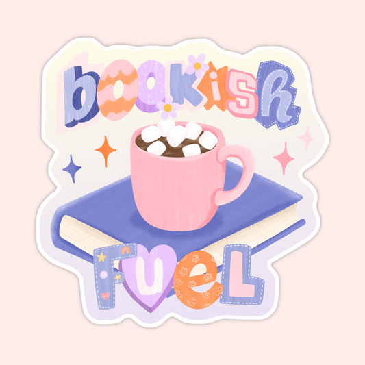 Pink mug of hot chocolate with marshmallows sitting on top of a book with the phrase “bookish fuel” in colorful playful lettering.
