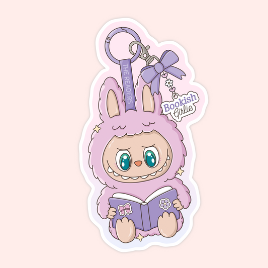 Cute purple Labubu monster holding a book with a bow keychain that says “The Readers” and “Bookish Girlie.”