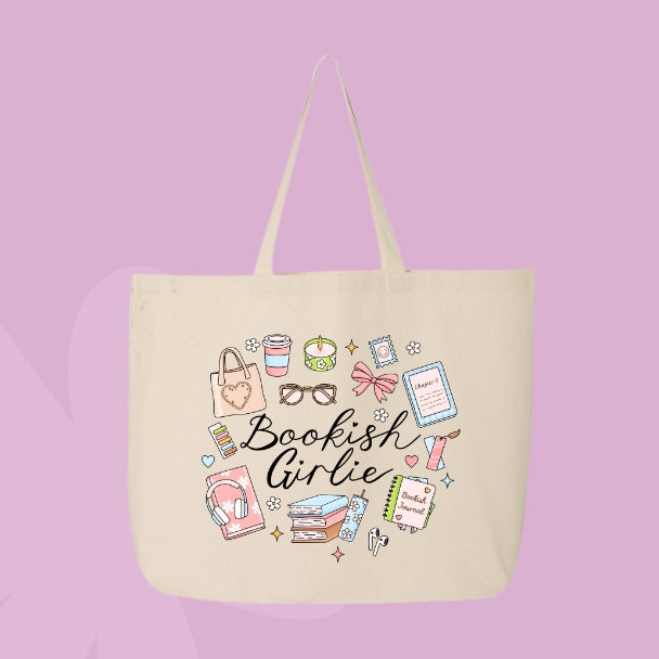 Beige tote bag with doodles of cozy items like books, coffee, candles, bows, glasses, and text that says “Bookish Girlie.”
