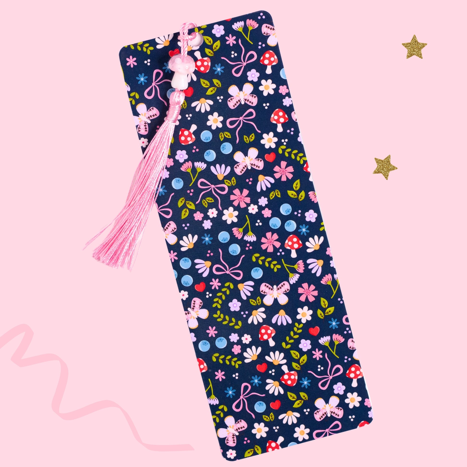 blue floral bow bookmark with flowers mushrooms and pink tassel on pink background