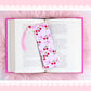 cherry coquette bookmark with bows and flowers placed on open book with pink aesthetic background
