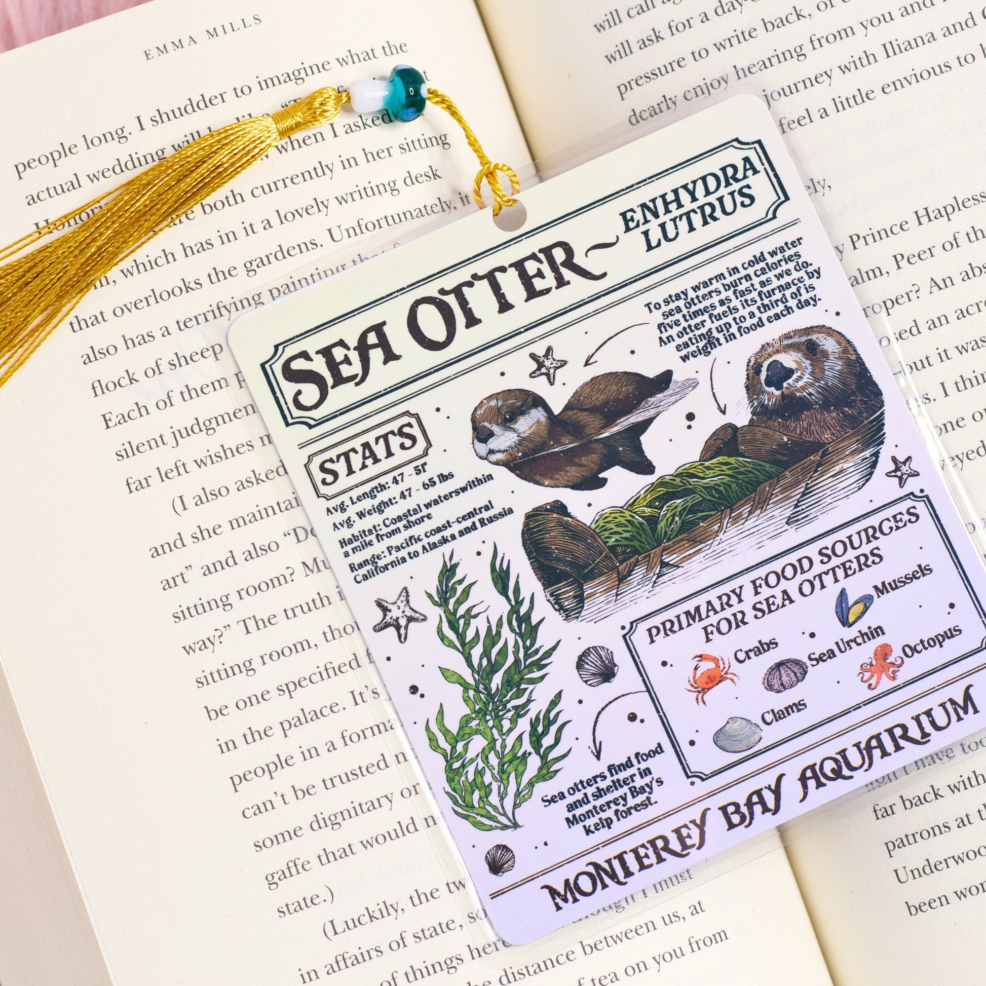 sea otter illustrated bookmark with vintage style marine design resting inside open book on pink background