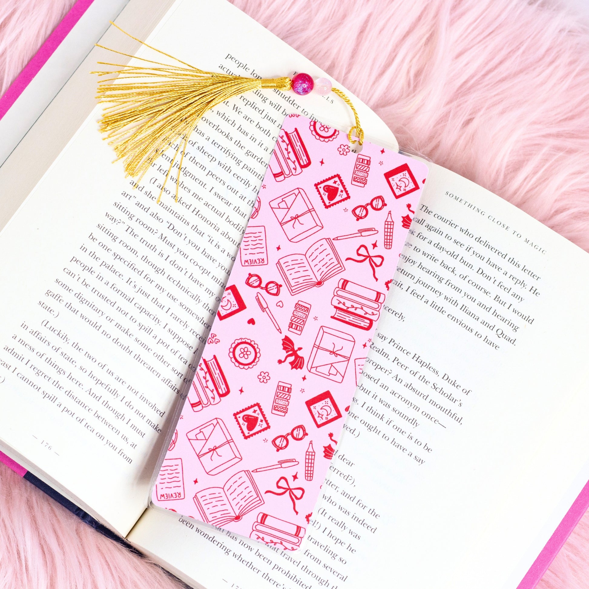 pink romance themed bookmark with bookish icons and gold tassel placed inside open book on pink background