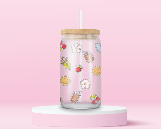 Glass cup with iced coffee cups, cherries, blue bows, tulips, strawberries, smiley faces, and white flowers scattered on a pink background.