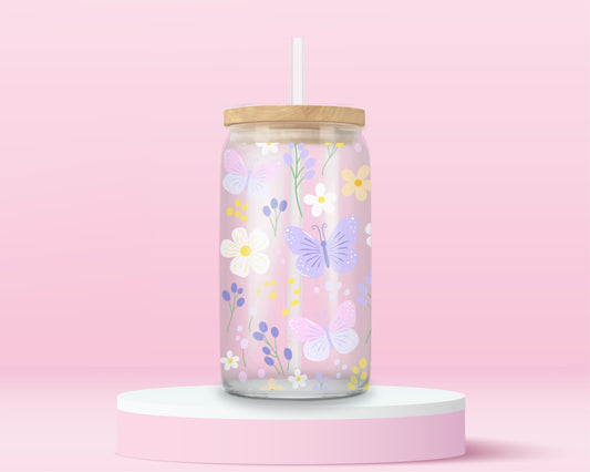 A pink glass cup decorated with pastel butterflies, daisies, and wildflowers in soft yellow, lilac, and white. A dreamy spring garden in glass form.