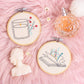 hand embroidered candle and open book wall art hoops on pink background with flowers and perfume styling