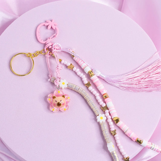 Pink capybara charm keychain with pastel flower beads, gold butterflies, and a pink tassel.