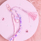 Handmade pastel beaded purse charm keychain with pink, purple, and iridescent beads displayed on a pink background