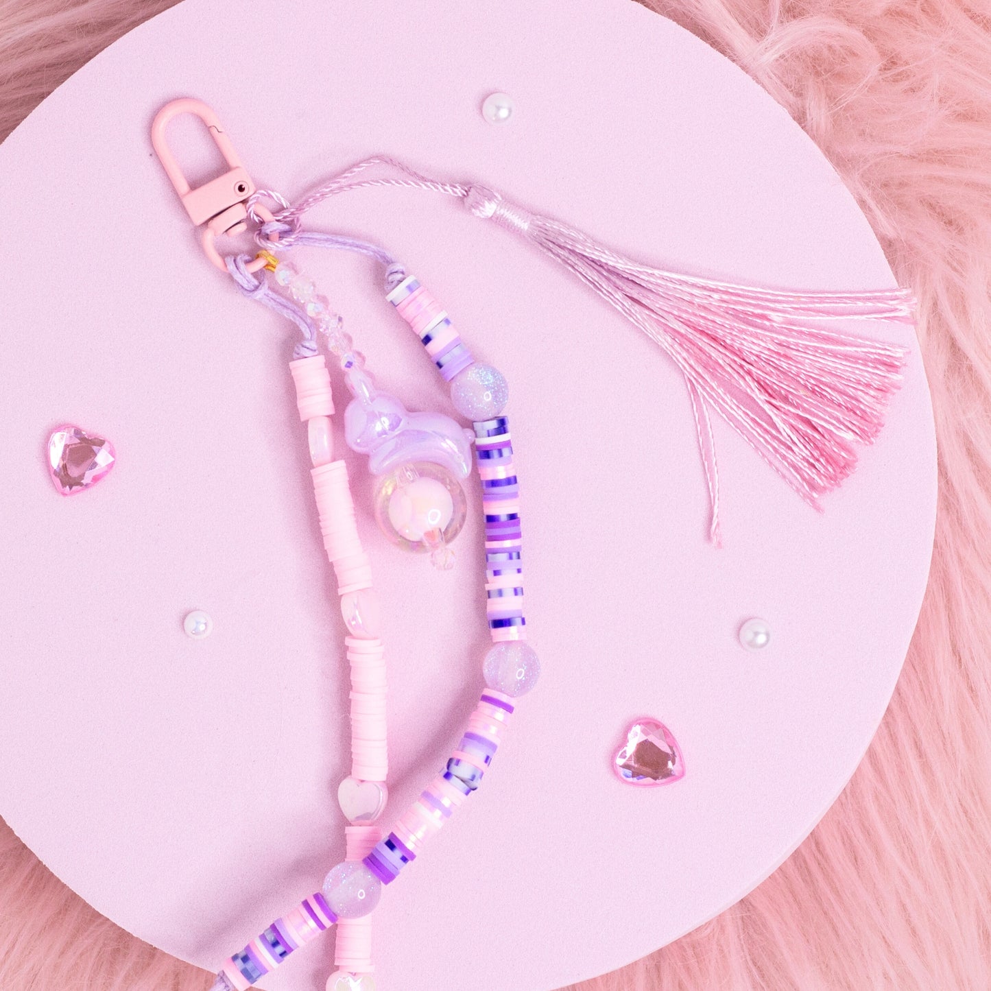 Handmade pastel beaded purse charm keychain with pink, purple, and iridescent beads displayed on a pink background