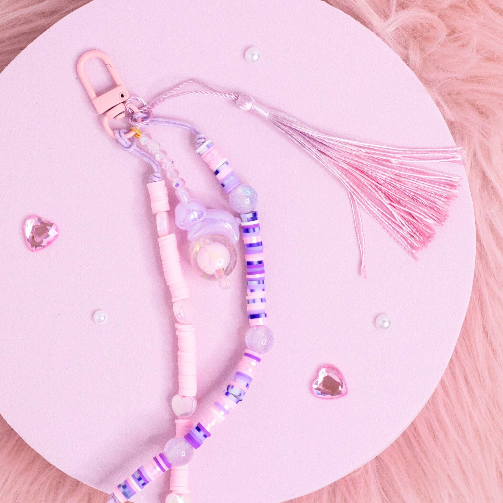 Handmade pastel beaded purse charm keychain with pink, purple, and iridescent beads displayed on a pink background