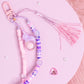 Close-up of pastel beaded purse charm keychain with glass orb charm, pink tassel, and purple bead details