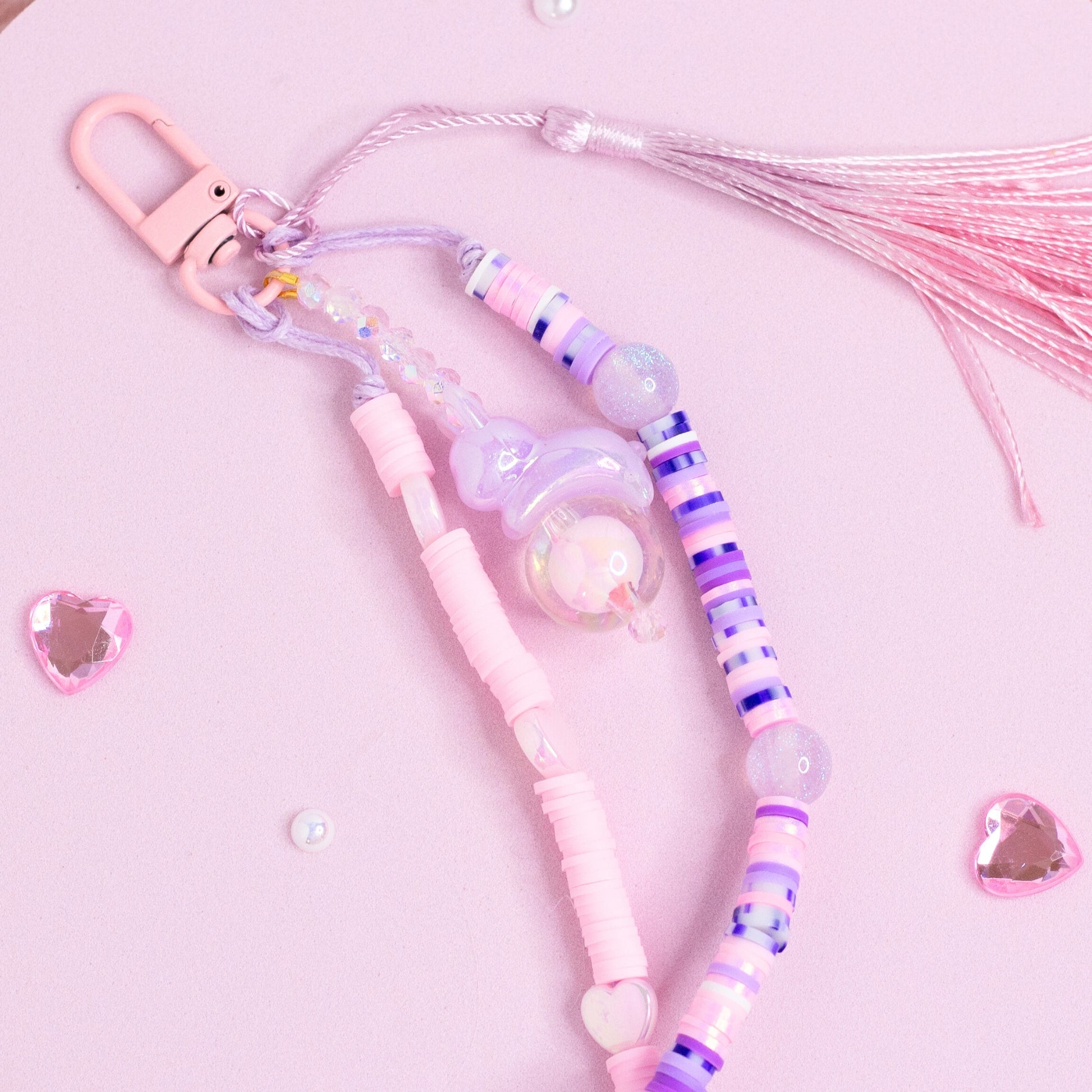 Cute pastel purse charm keychain with pink and purple beads, heart bead accents, and soft pink tassel on pink background