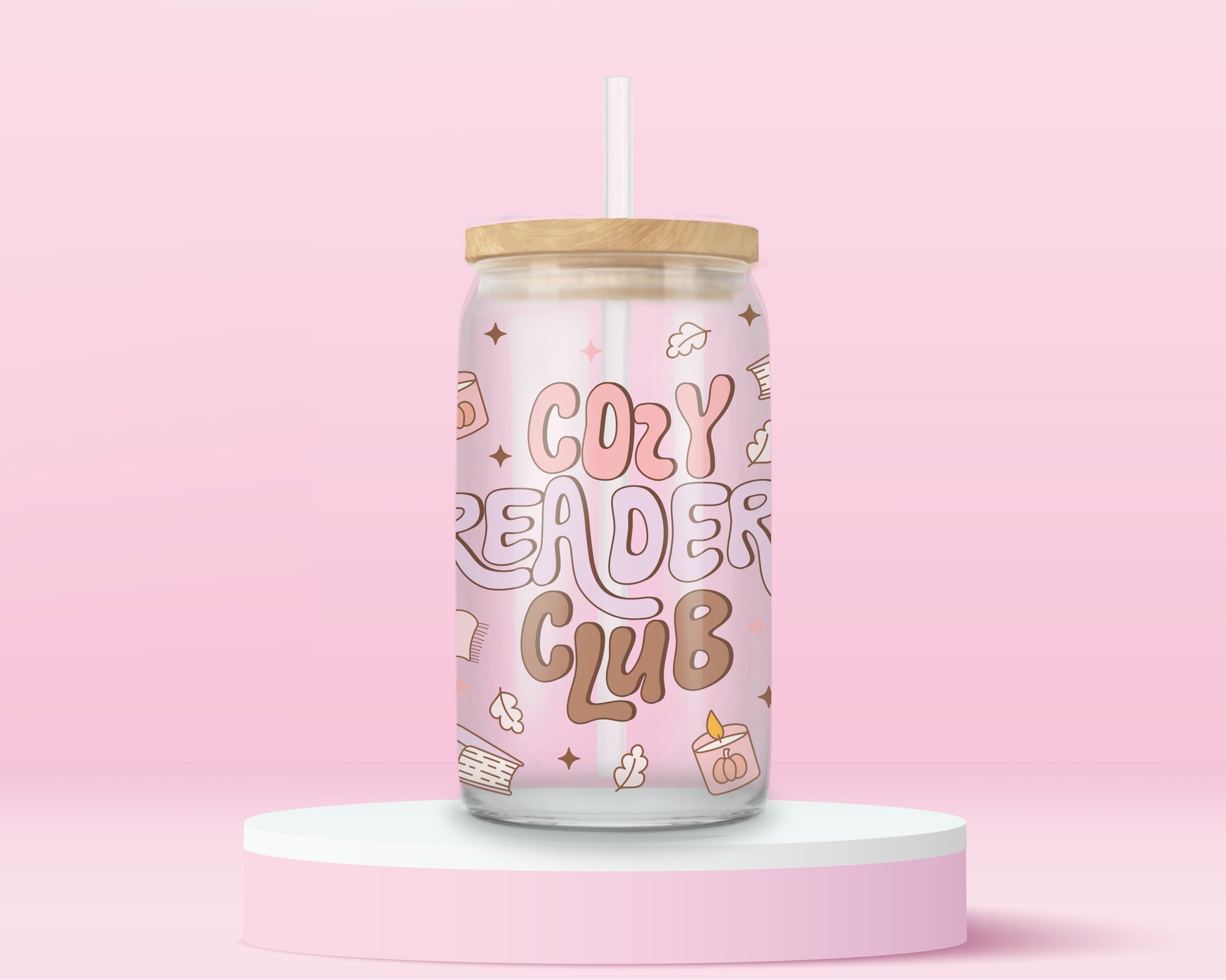 Pink glass tumbler with large retro text “Cozy Reader Club” surrounded by books, mugs, and candles, with bamboo lid and straw.