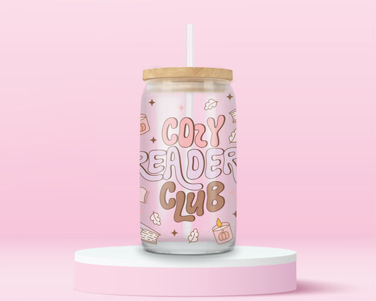 Pink glass tumbler with large retro text “Cozy Reader Club” surrounded by books, mugs, and candles, with bamboo lid and straw.