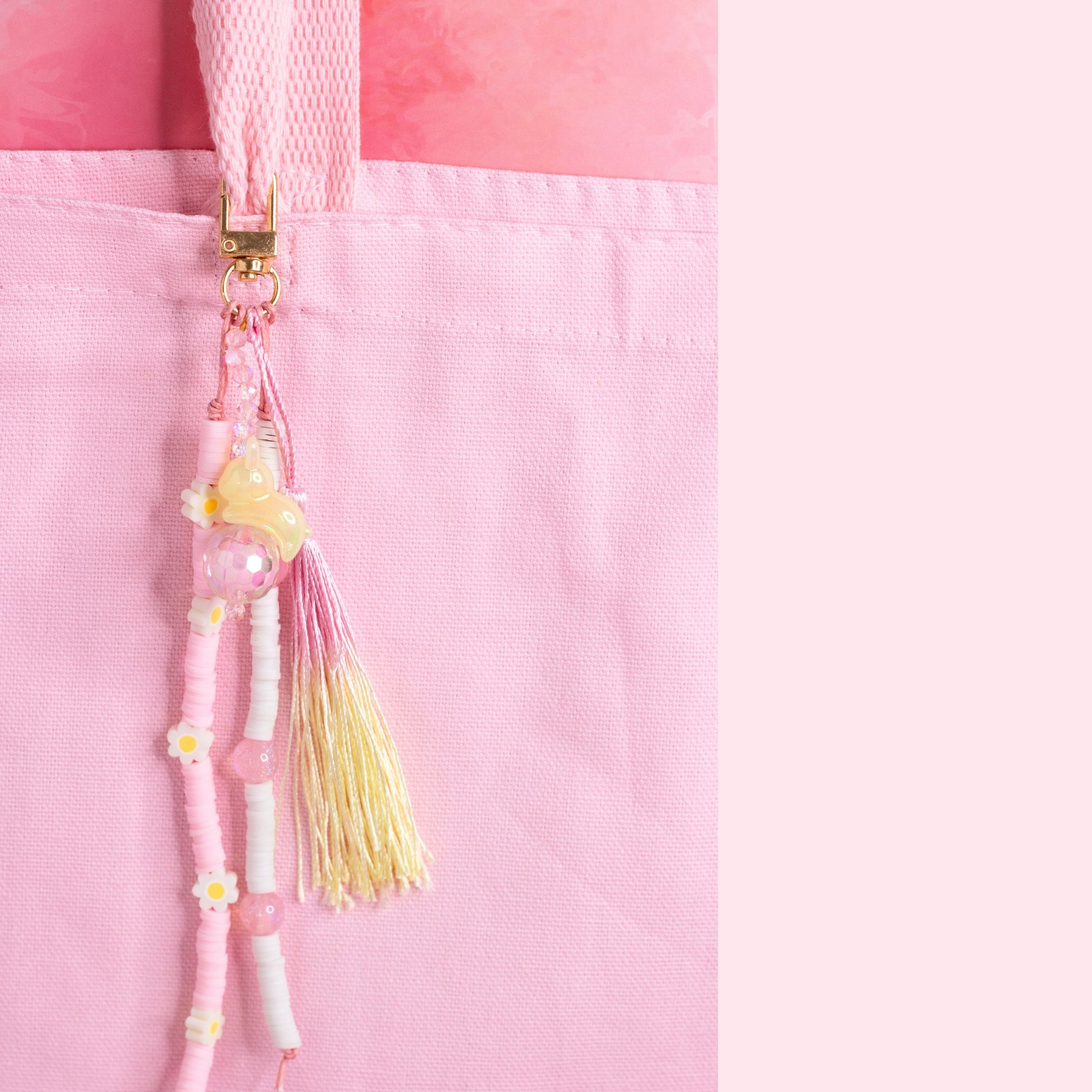 Pastel beaded purse charm keychain with bunny charm, daisy beads, and pink and yellow tassel clipped to a pink tote bag