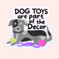 Gray and black dog lying with tennis ball and rope toys and text that reads “Dog toys are part of the decor.”