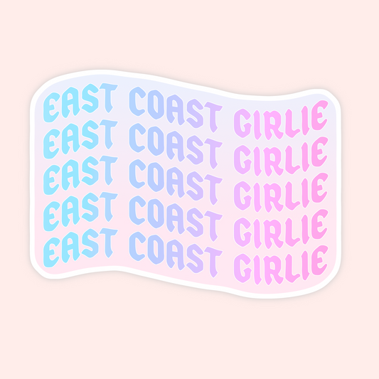 A die-cut sticker with a wavy flag-like shape featuring the phrase 'EAST COAST GIRLIE' repeated five times in a pastel gradient. The text transitions from light blue to lavender to pink, and the sticker has a white border on a pale pink background.