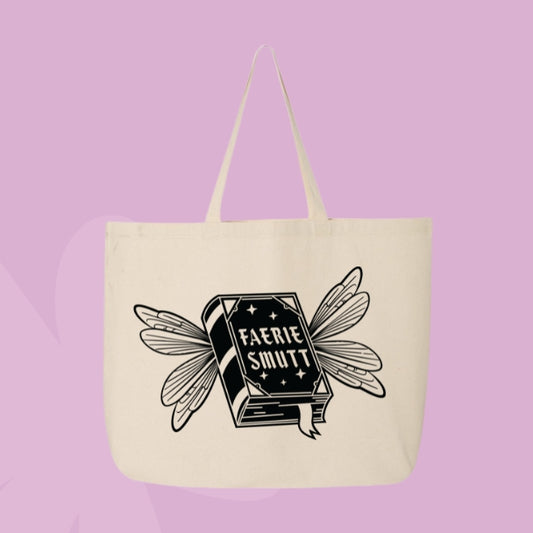 Beige tote bag with a black illustration of a fantasy book with fairy wings, labeled “Faerie Smut.”