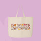 Large beige canvas tote bag featuring the words farmers market girlie surrounded by jam, bread, mushrooms, produce, cheese, flowers, and market-inspired doodles.