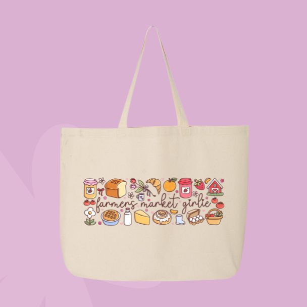 Large beige canvas tote bag featuring the words farmers market girlie surrounded by jam, bread, mushrooms, produce, cheese, flowers, and market-inspired doodles.