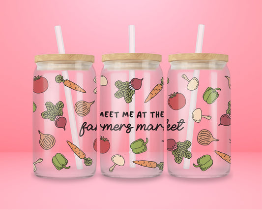 Glass cup with pink background decorated with hand-drawn vegetables like tomatoes, carrots, onions, and text that reads “meet me at the farmers market.”