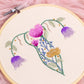 Close-up of floral uterus embroidery hoop art with pink and purple hand embroidered flowers on natural cotton fabric