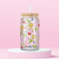 Glass cup with pink background covered in colorful fruits (watermelon, strawberries, blueberries, cherries) and spring flowers (daisies, tulips, daffodils).