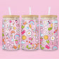 Glass can tumbler with bamboo lid and glass straw featuring colourful doodles including bows, rainbows, mushrooms, daisies, stars, hearts, bubbles, and butterflies on a pink background.