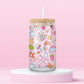 Glass can tumbler with bamboo lid and glass straw featuring colourful doodles including bows, rainbows, mushrooms, daisies, stars, hearts, bubbles, and butterflies on a pink background.