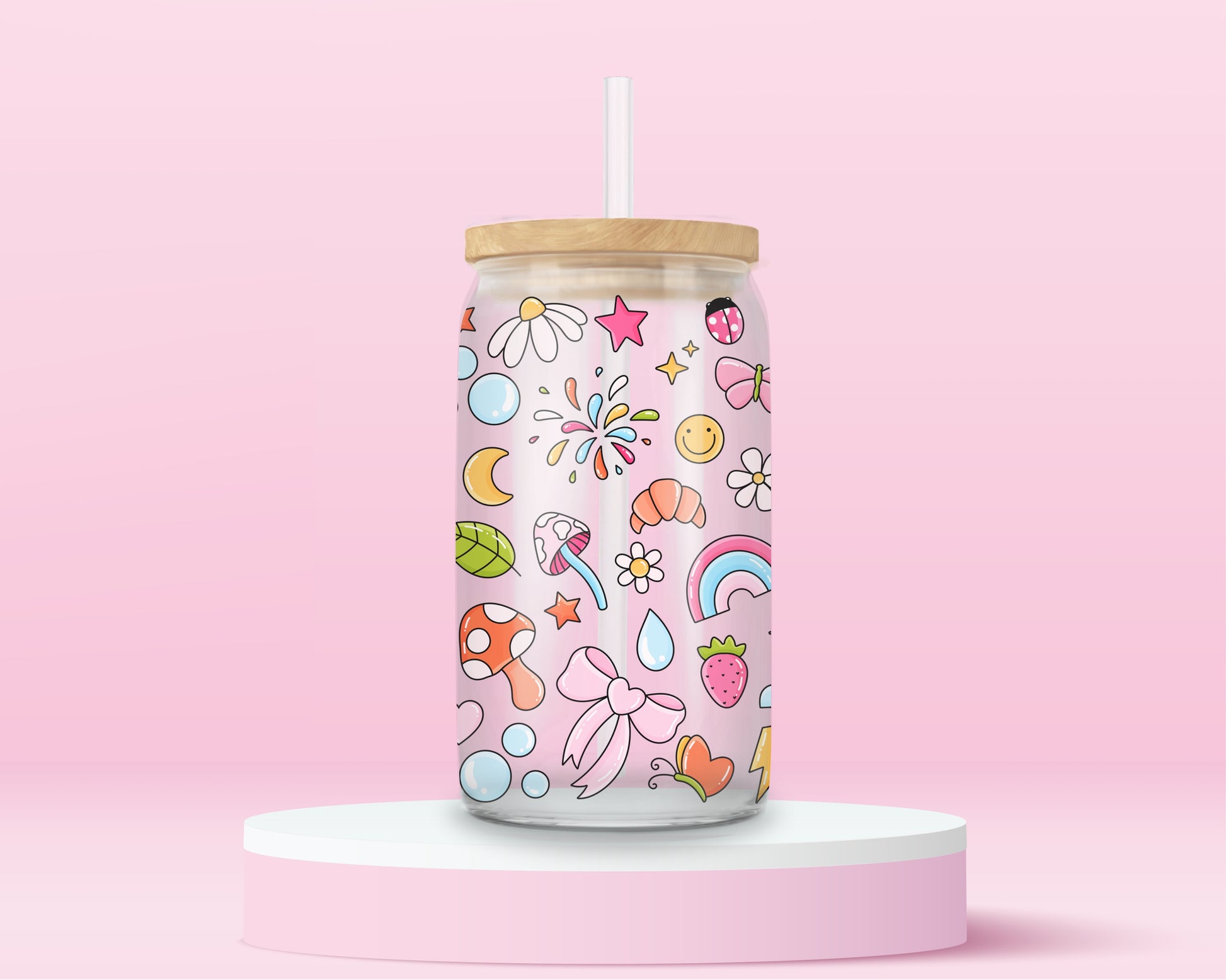Glass can tumbler with bamboo lid and glass straw featuring colourful doodles including bows, rainbows, mushrooms, daisies, stars, hearts, bubbles, and butterflies on a pink background.