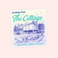 Postcard-style illustrated cottage sticker with forest scenery and the phrase “Greetings From the Cottage,” inspired by Heated Rivalry and summer romance settings.